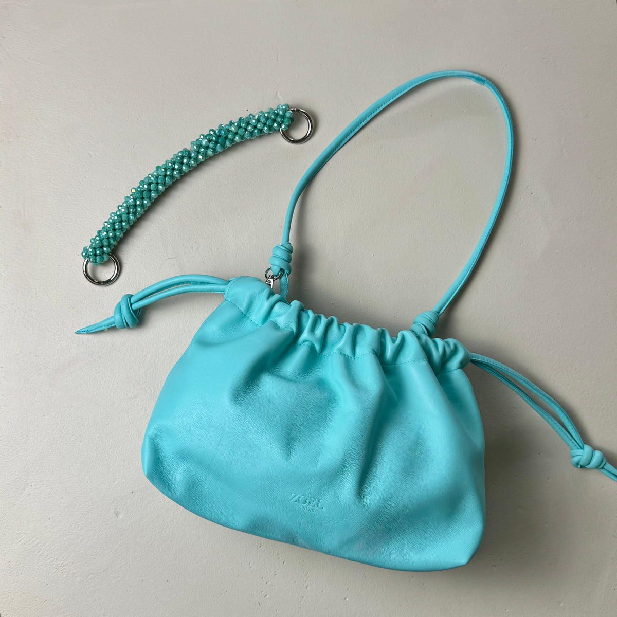 Turquoise leather pouch bag from ZOEL with detachable leather shoulder strap and detachable crystal beaded handle.
