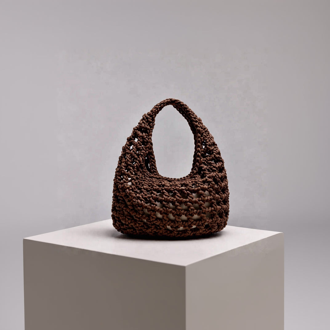 A chocolate brown crocheted shoulder bag with a slouchy, open-knit texture and a single integrated handle. Designed by ZOEL for summer strolls from day to night.