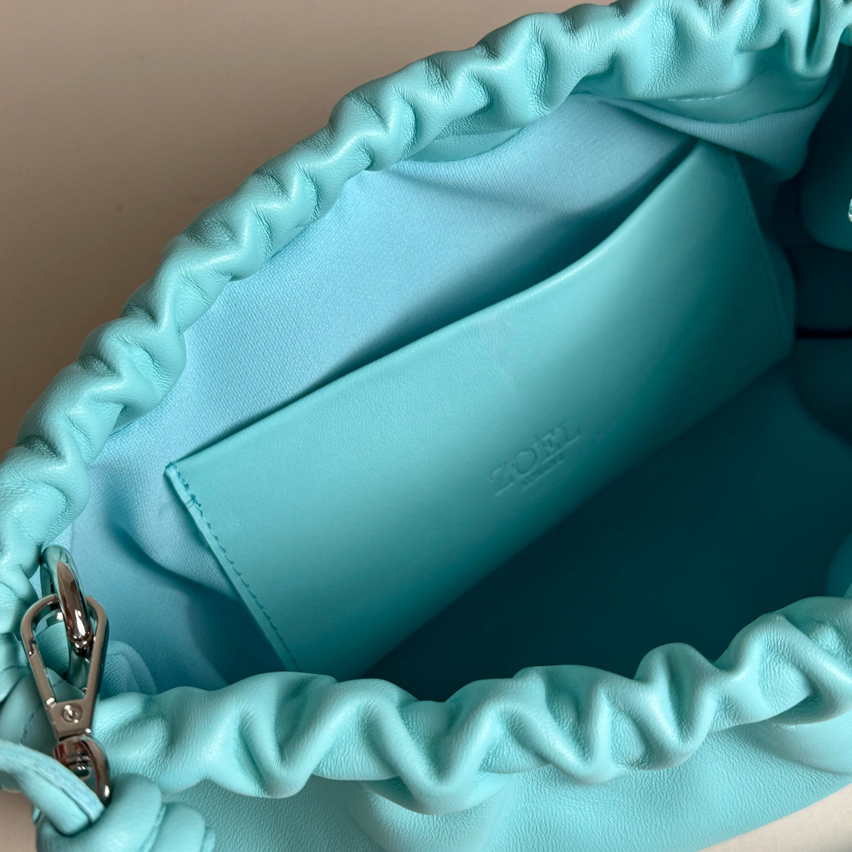 Close-up of the interior of a turquoise  leather pouch bag from ZOEL, showing its fabric lining and leather inside pocket. 