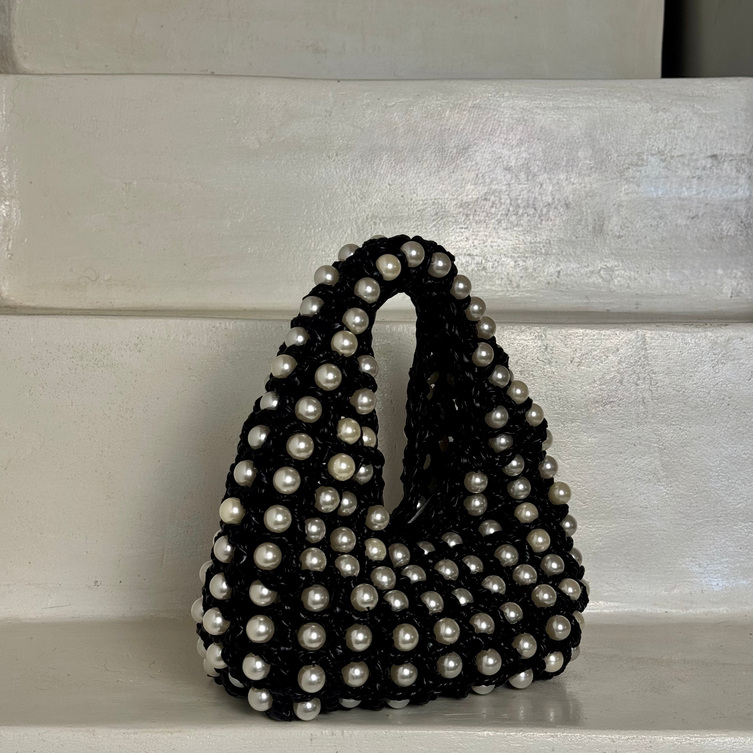 A black beaded handbag covered in white faux pearls, standing on a white painted wooden stepMade by Zoel